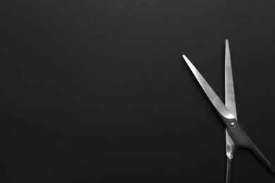 Photo of Pair of sharp scissors on dark background, top view. Space for text