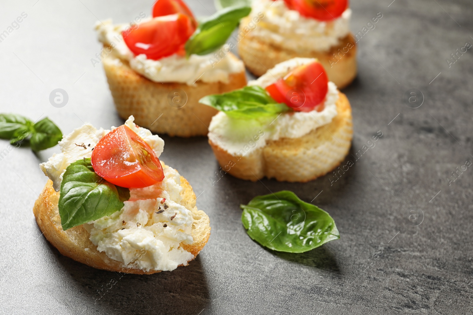 Photo of Pieces of baguette with tasty cream cheese and tomatoes on gray table