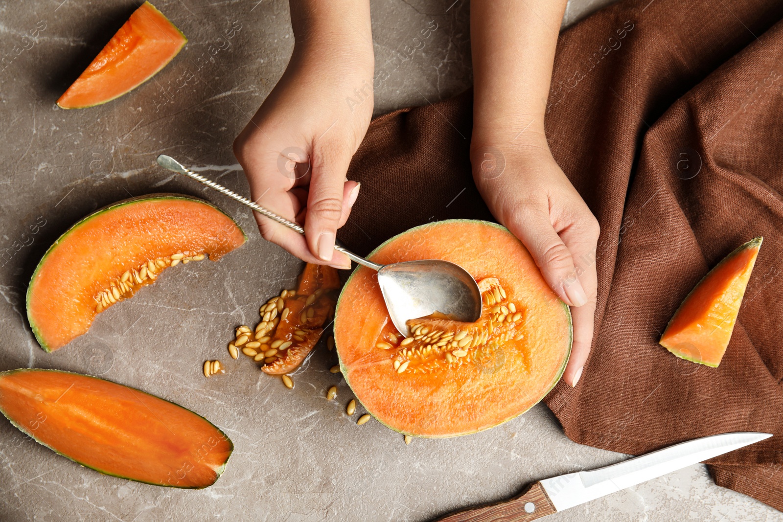 Photo of Young woman removing seeds from ripe melon with spoon at beige marble table, top view