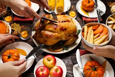 People eating traditional cooked turkey at wooden table, closeup. Thanksgiving day celebration