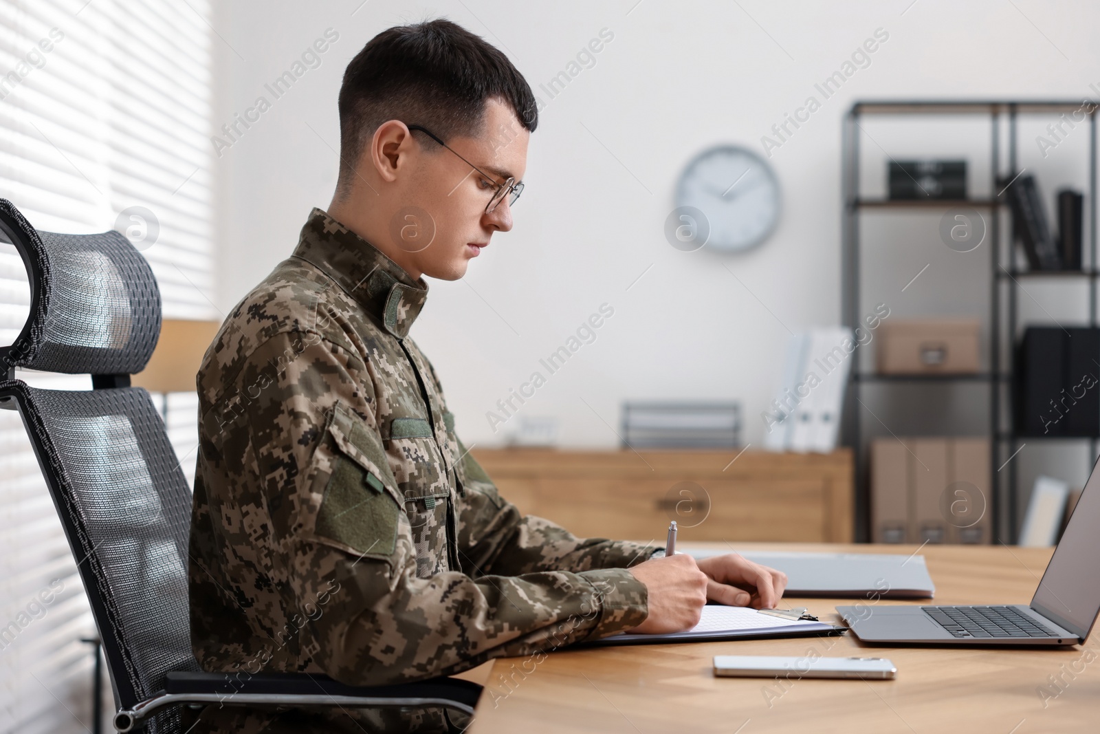 Photo of Military service. Young soldier working at wooden table in office