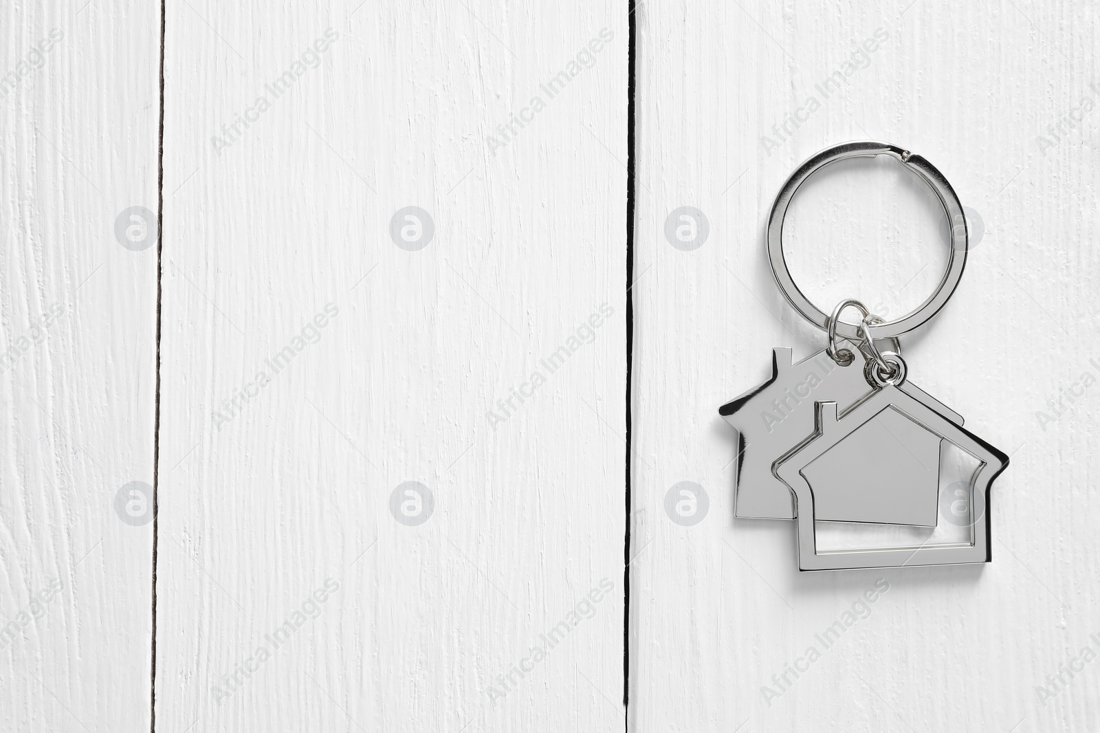 Photo of Metal keychain in shape of houses on white wooden table, top view. Space for text