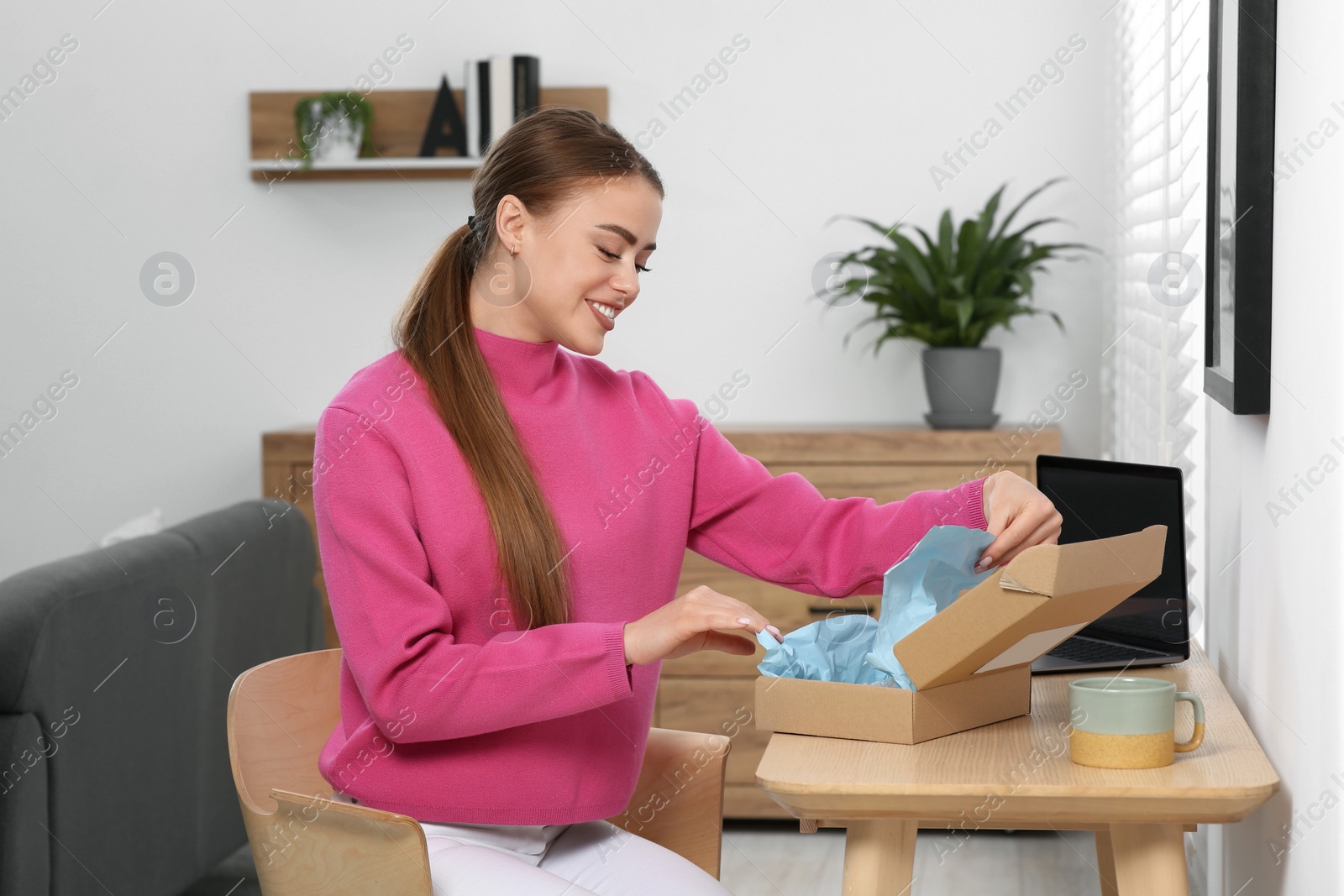 Photo of Happy woman unpacking parcel at home. Online store
