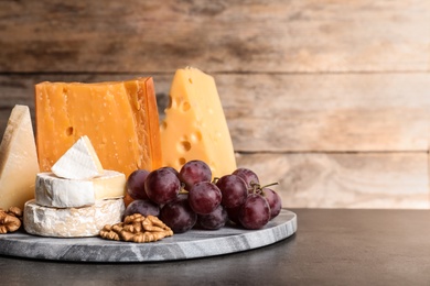 Composition with assorted cheese, grapes and walnuts on table against wooden background, space for text