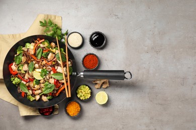 Photo of Stir-fry. Tasty noodles with meat in wok, chopsticks and ingredients on grey textured table, flat lay. Space for text