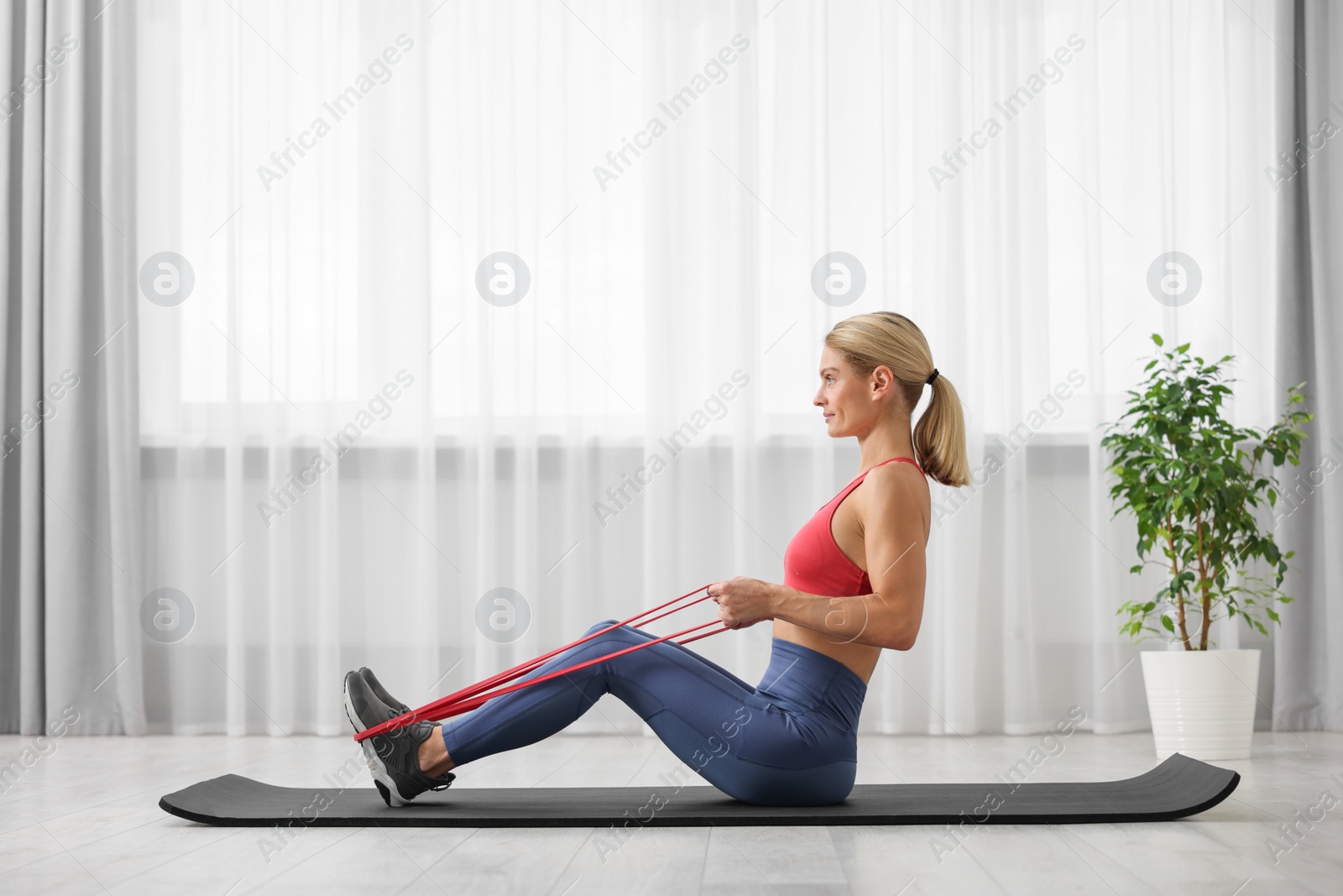 Photo of Fit woman doing exercise with fitness elastic band on mat at home