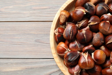 Photo of Delicious roasted edible chestnuts on wooden table, top view. Space for text