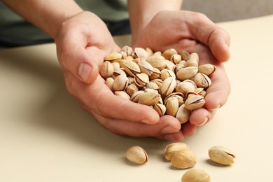 Woman holding tasty roasted pistachio nuts on beige background, closeup