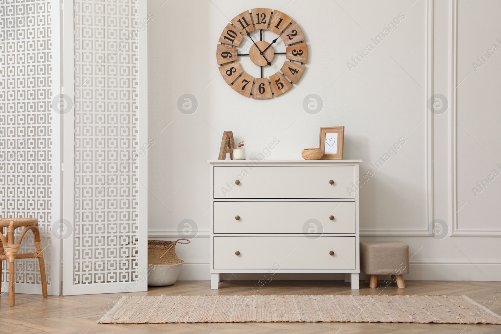 Photo of Stylish room with wooden folding screen and chest of drawers near white wall. Interior design