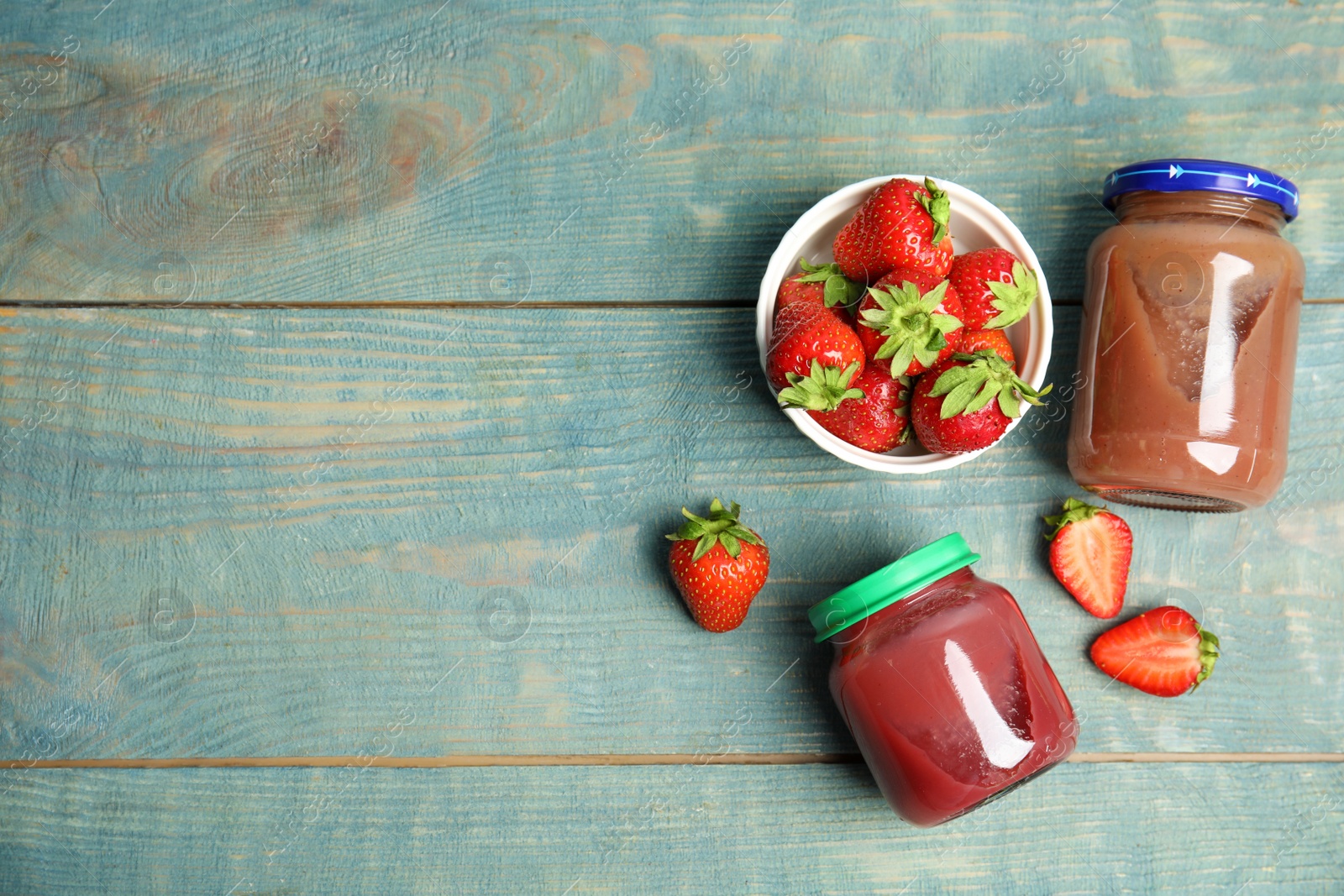 Photo of Jars with baby food and fresh strawberries on light blue wooden table, flat lay. Space for text