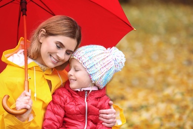 Mother and daughter with umbrella in autumn park on rainy day