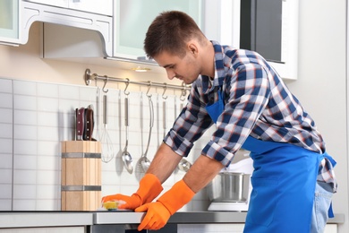 Photo of Man cleaning kitchen stove with sponge in house