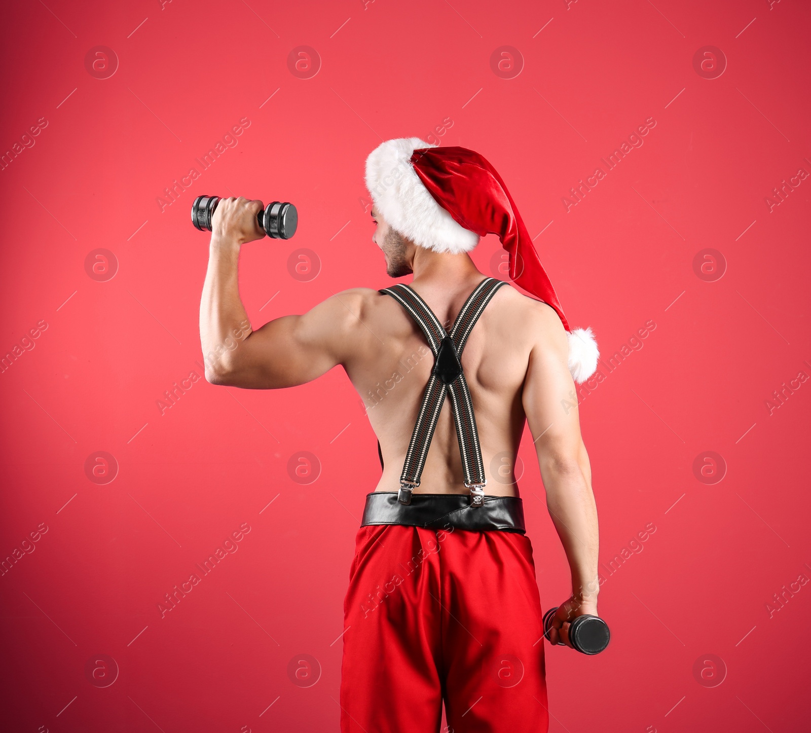 Photo of Shirtless sexy young Santa Claus with dumbbells on color background