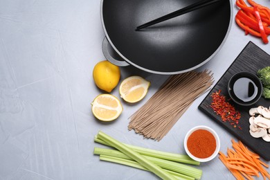 Photo of Wok, chopsticks and different products on grey table, flat lay. Space for text