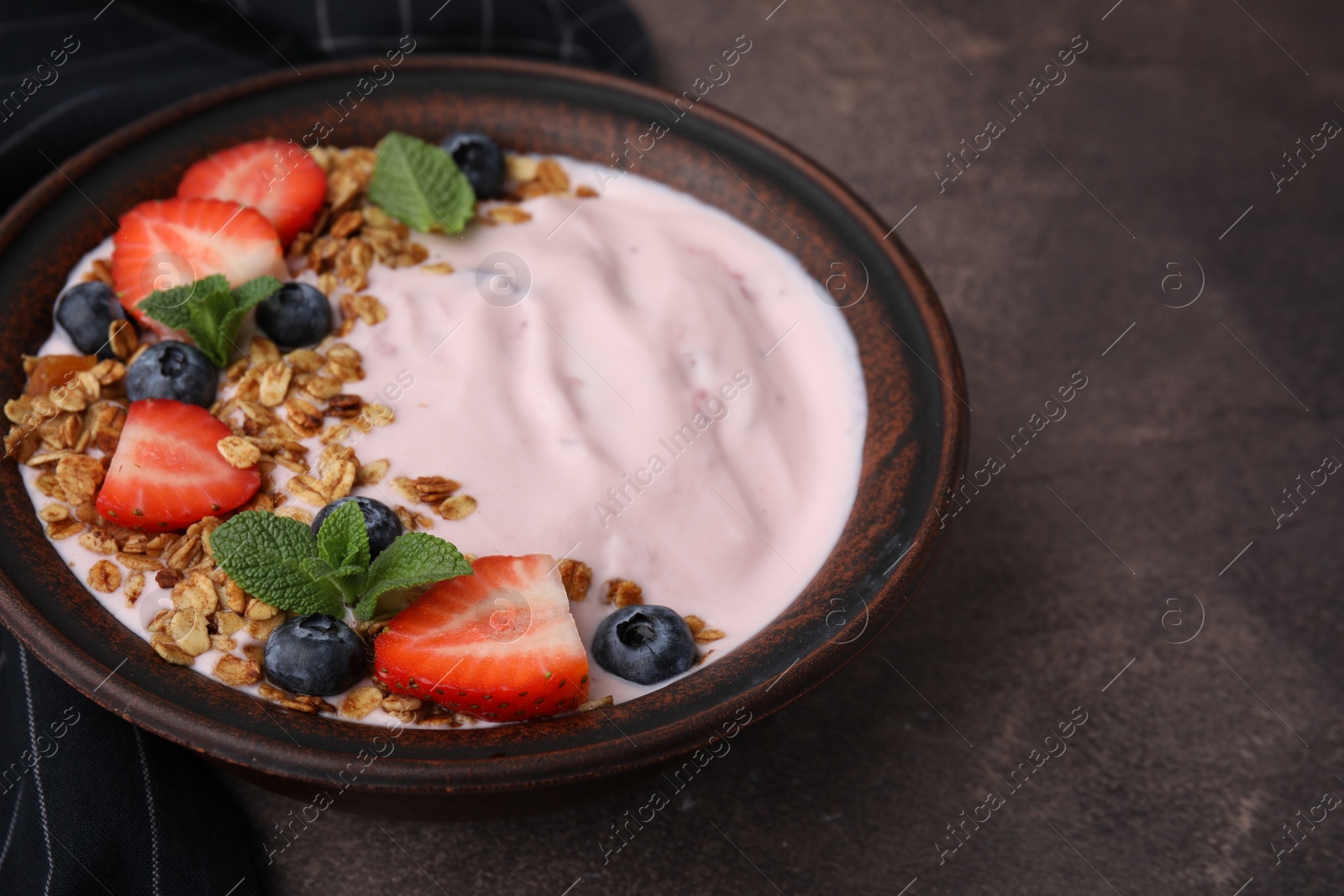 Photo of Bowl with yogurt, berries and granola on brown table. Space for text