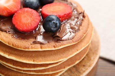 Photo of Tasty pancakes with chocolate paste and berries on wooden table, closeup