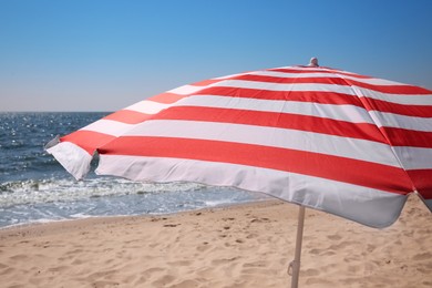 Photo of Red and white striped beach umbrella on sandy seashore