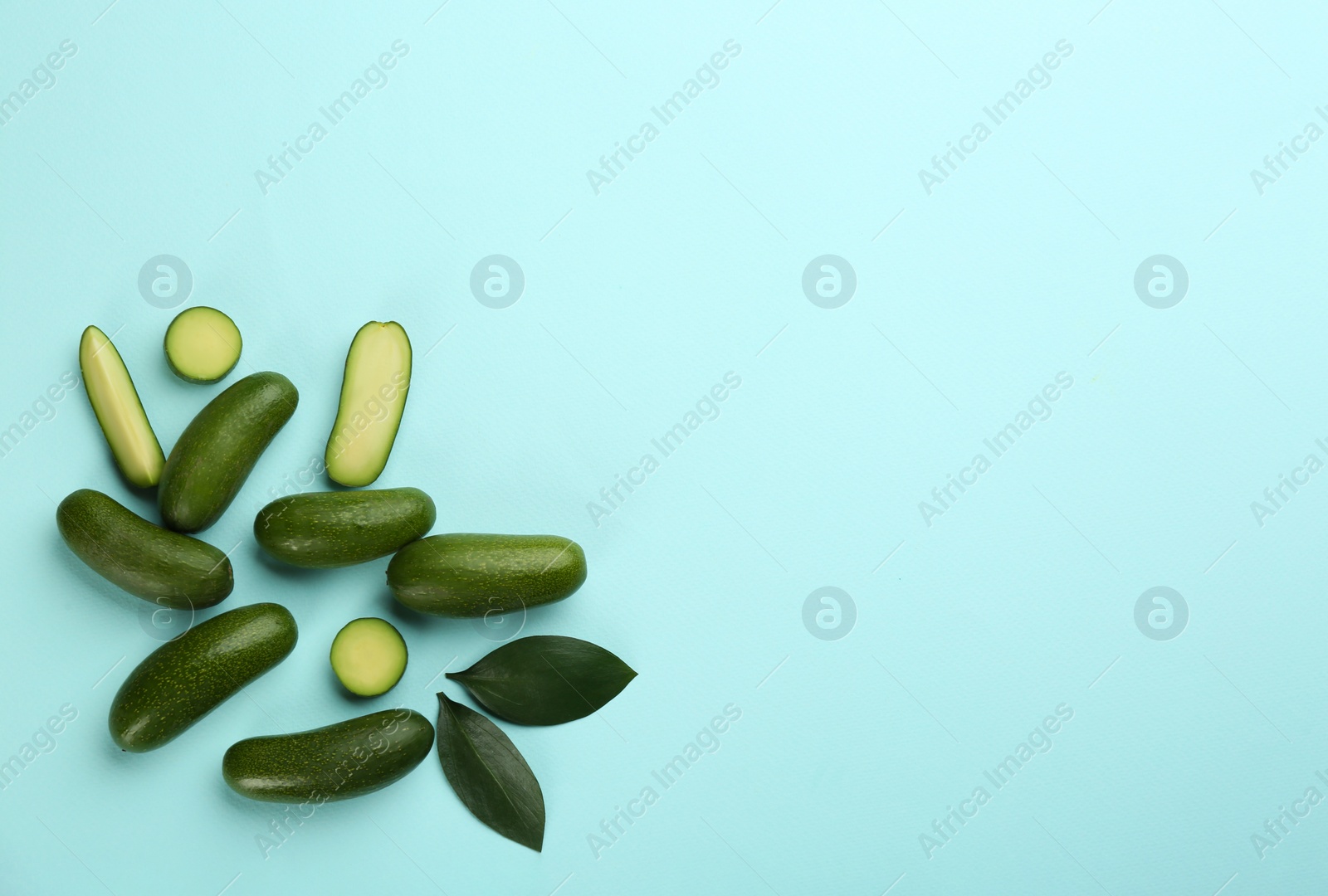 Photo of Whole and cut seedless avocados with green leaves on light blue background, flat lay. Space for text