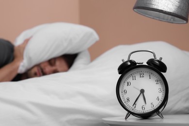 Sleepy man covering his ears with pillows in bed, focus on alarm clock. Space for text