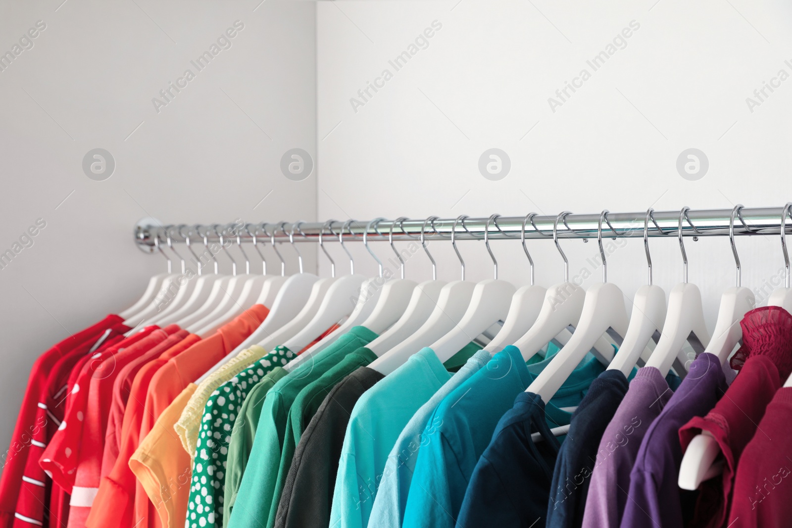 Photo of Hangers with different colorful clothes on rack in wardrobe