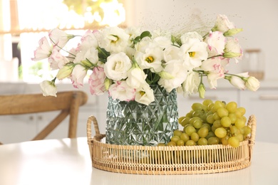 Bouquet of beautiful eustoma flowers and grapes on white table in kitchen. Interior design