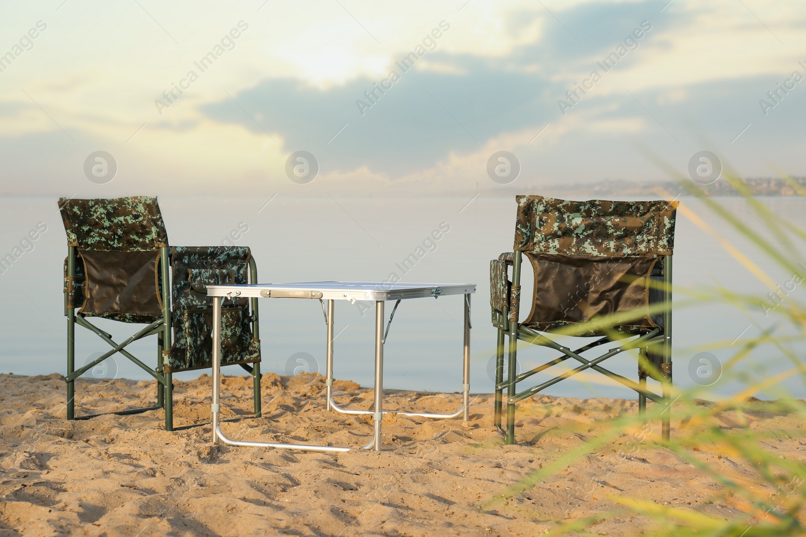 Photo of Camouflage fishing chairs and table on sandy beach near river