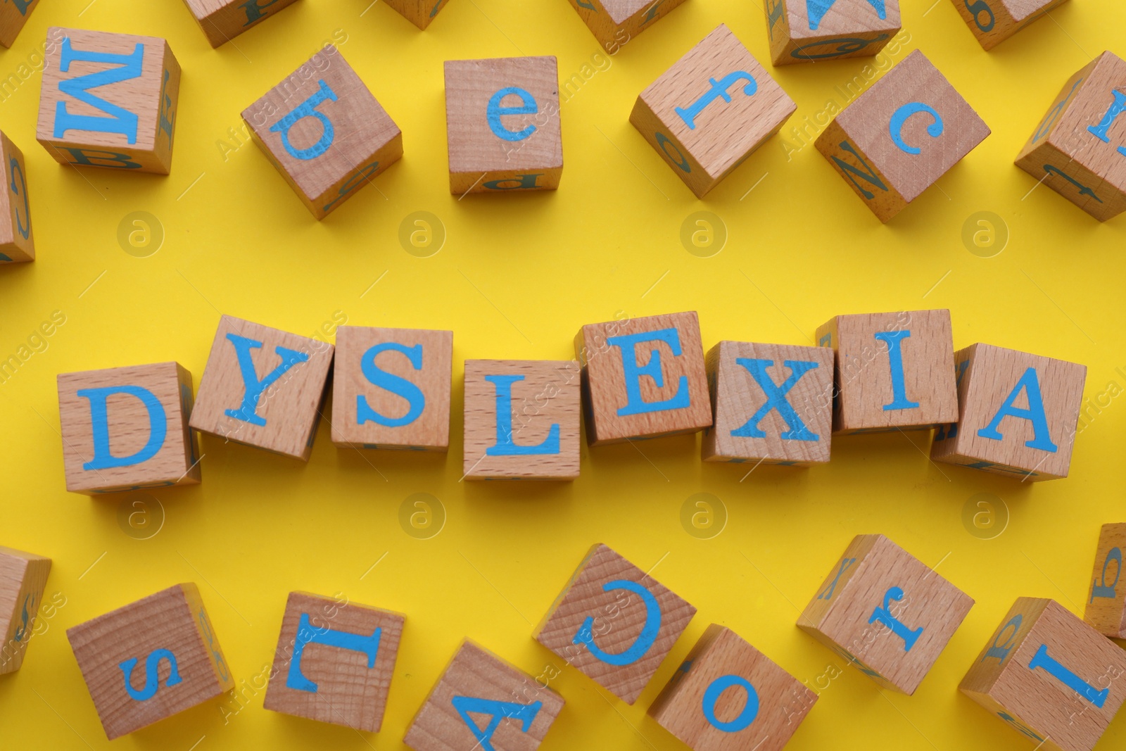 Photo of Wooden cubes with word Dyslexia on yellow background, flat lay