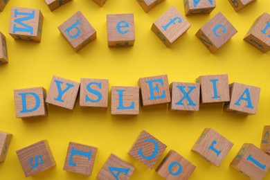 Wooden cubes with word Dyslexia on yellow background, flat lay