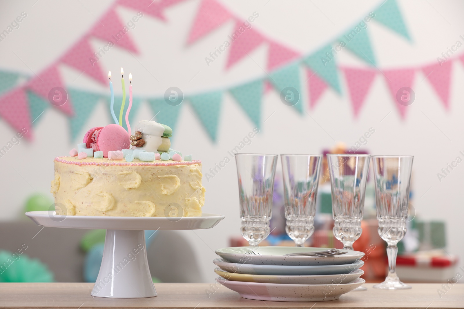 Photo of Delicious cake decorated with macarons and marshmallows and clean tableware on wooden table in festive room