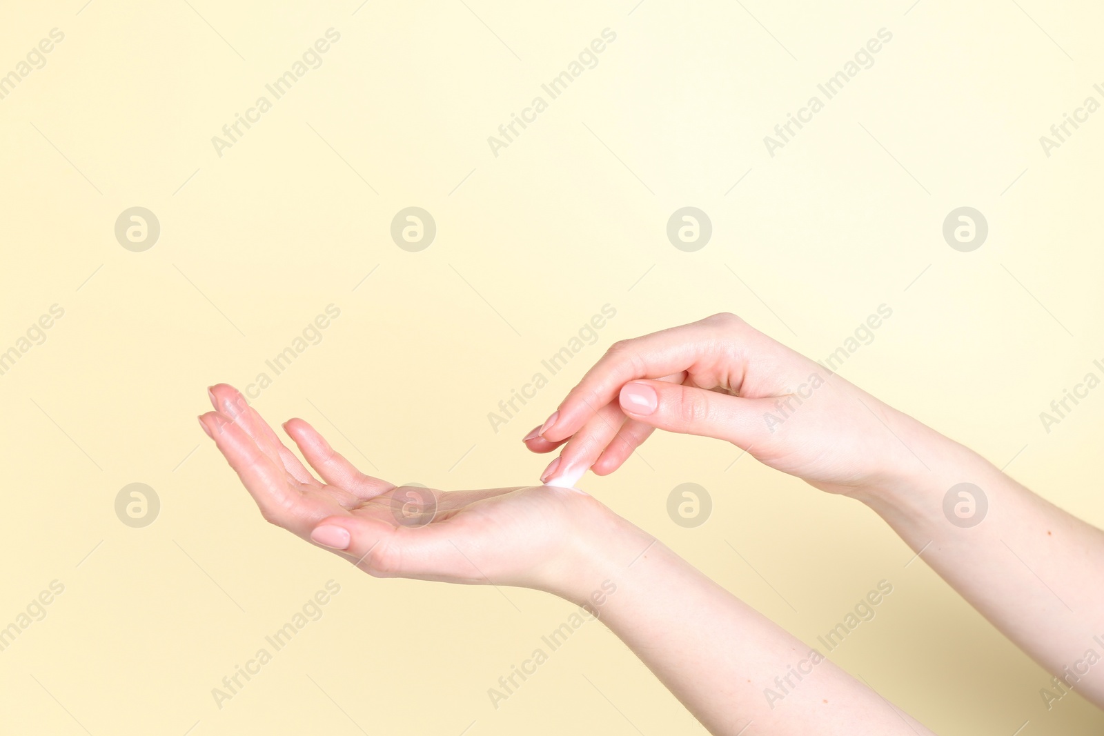 Photo of Woman applying cream on her hand against yellow background, closeup