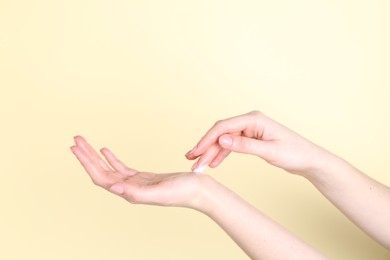 Woman applying cream on her hand against yellow background, closeup