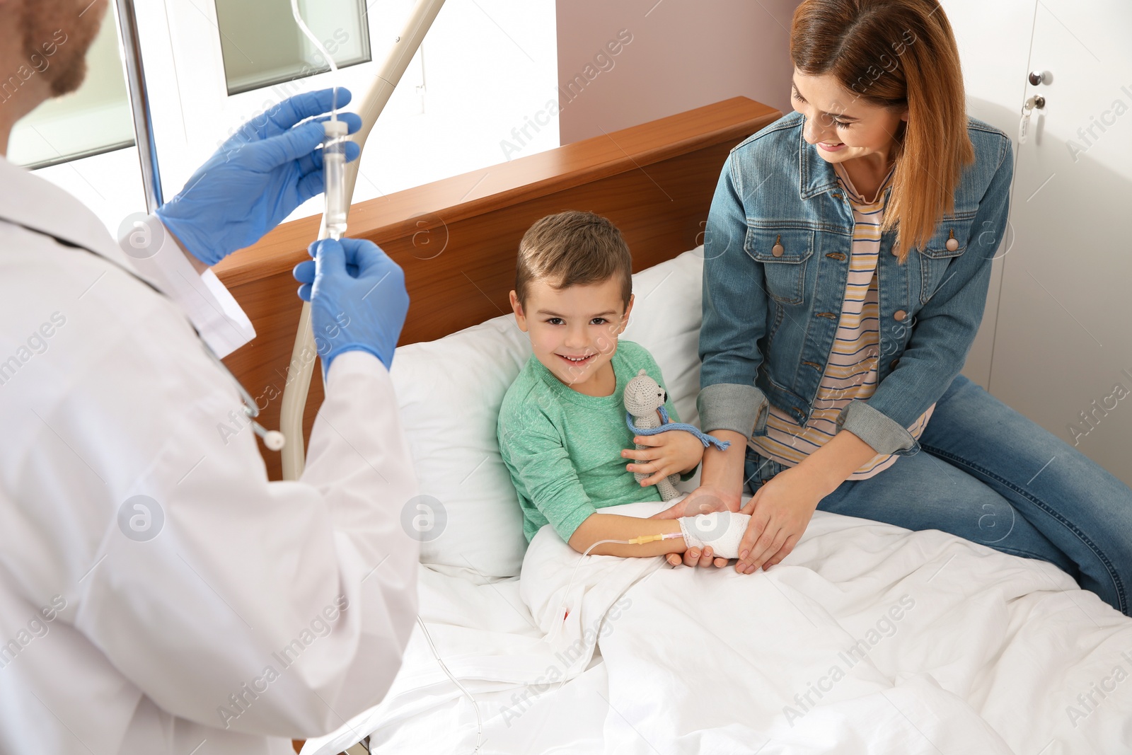 Photo of Doctor adjusting intravenous drip for little child in hospital during parent's visit