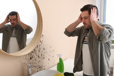 Shocked man looking at affected with mold walls in bathroom