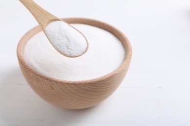 Photo of Taking baking soda from bowl at white wooden table, closeup. Space for text