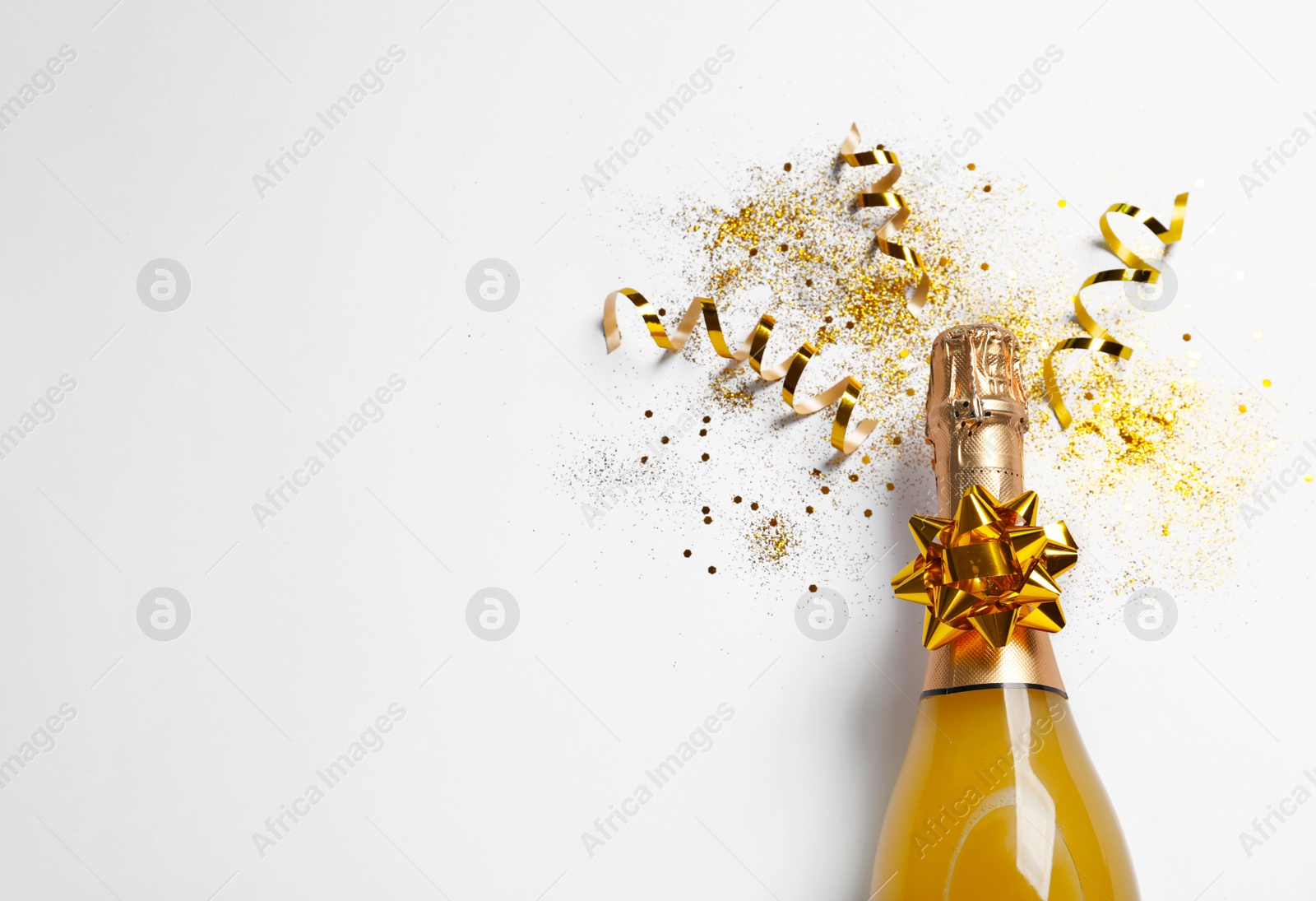 Photo of Bottle of champagne with gold glitter, confetti and space for text on white background, top view. Hilarious celebration