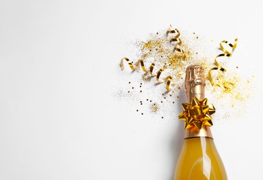 Bottle of champagne with gold glitter, confetti and space for text on white background, top view. Hilarious celebration