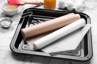 Photo of Baking pan with parchment paper, different ingredients and kitchen tools on white marble table