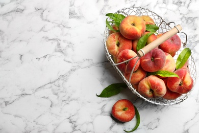 Photo of Fresh ripe donut peaches with leaves on white marble table, flat lay. Space for text