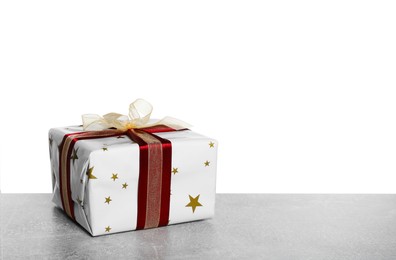 Photo of Christmas gift wrapped in star patterned paper on grey table against white background. Space for text