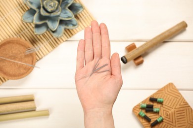 Woman holding many acupuncture needles over white wooden table, top view