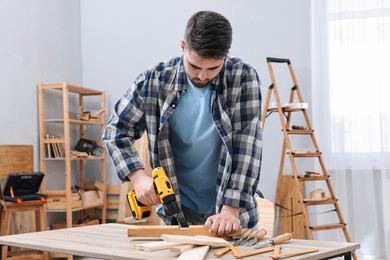 Photo of Young handyman working with electric drill at table in workshop