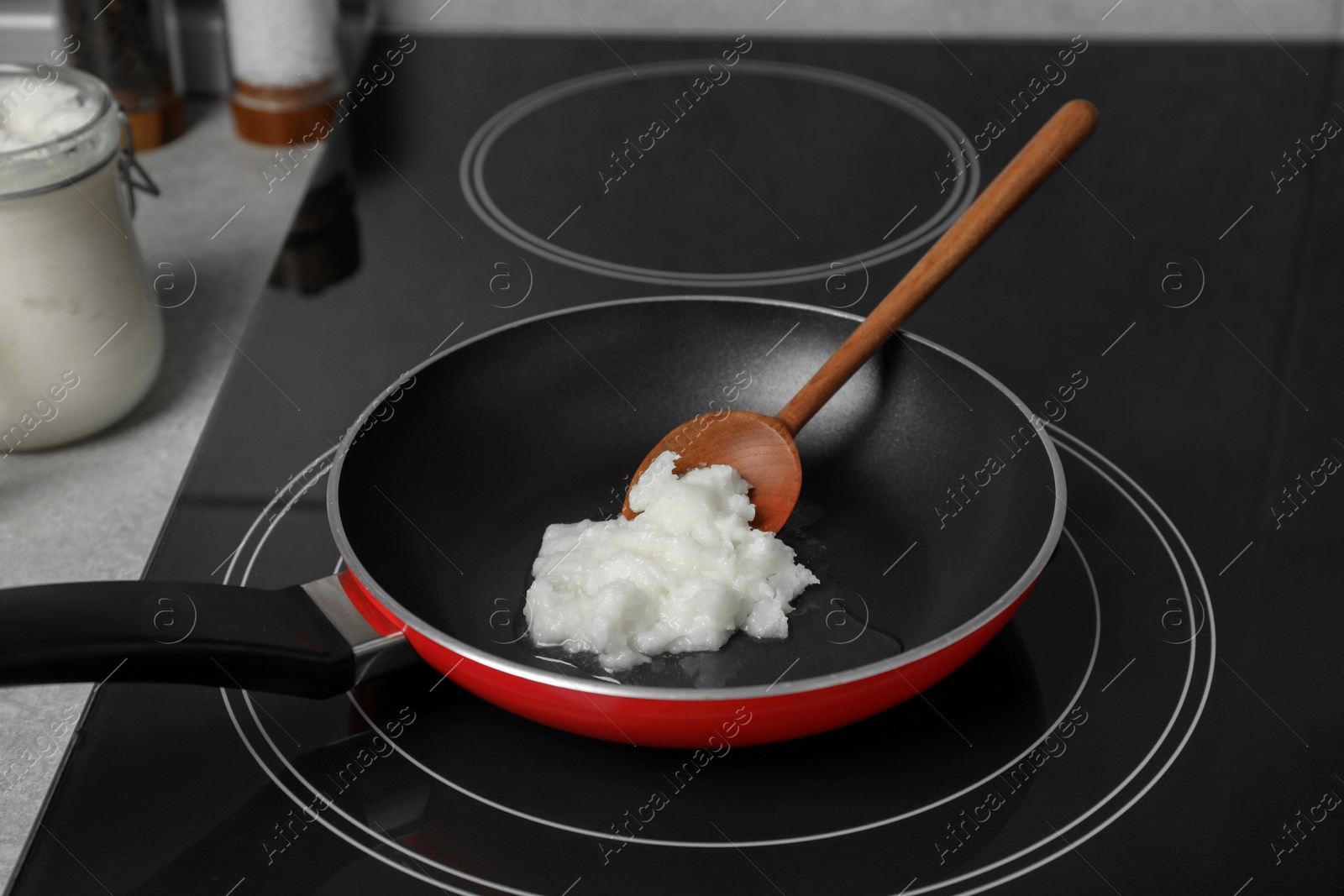 Photo of Frying pan with coconut oil and wooden spatula on induction stove. Healthy cooking