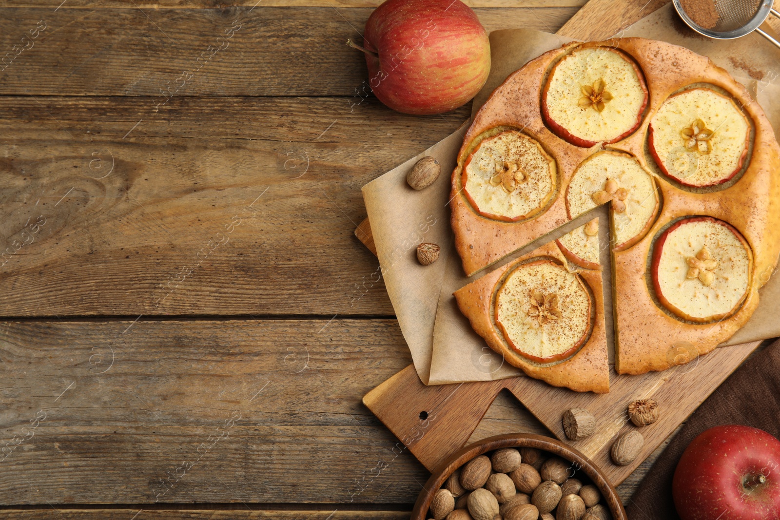 Photo of Nutmeg seeds, tasty apple pie and fresh fruits on wooden table, flat lay. Space for text