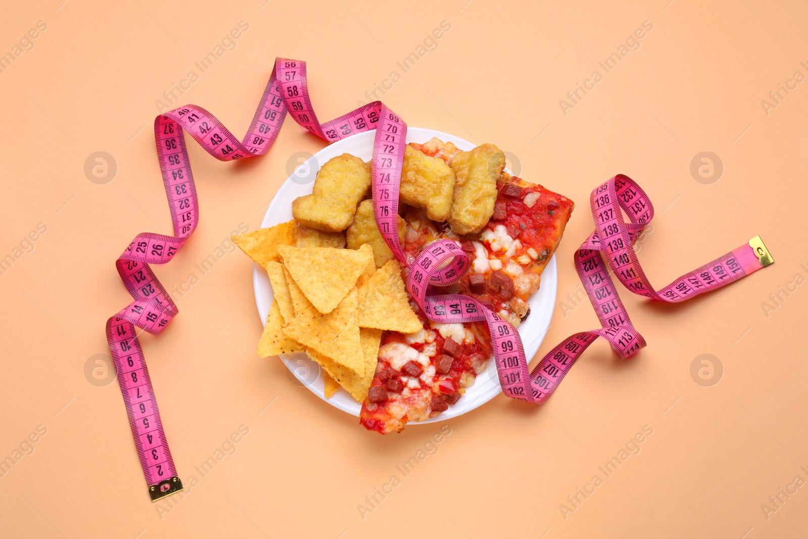 Photo of Chips, chicken nuggets, pizza with measuring tape on orange background, flat lay. Diet concept