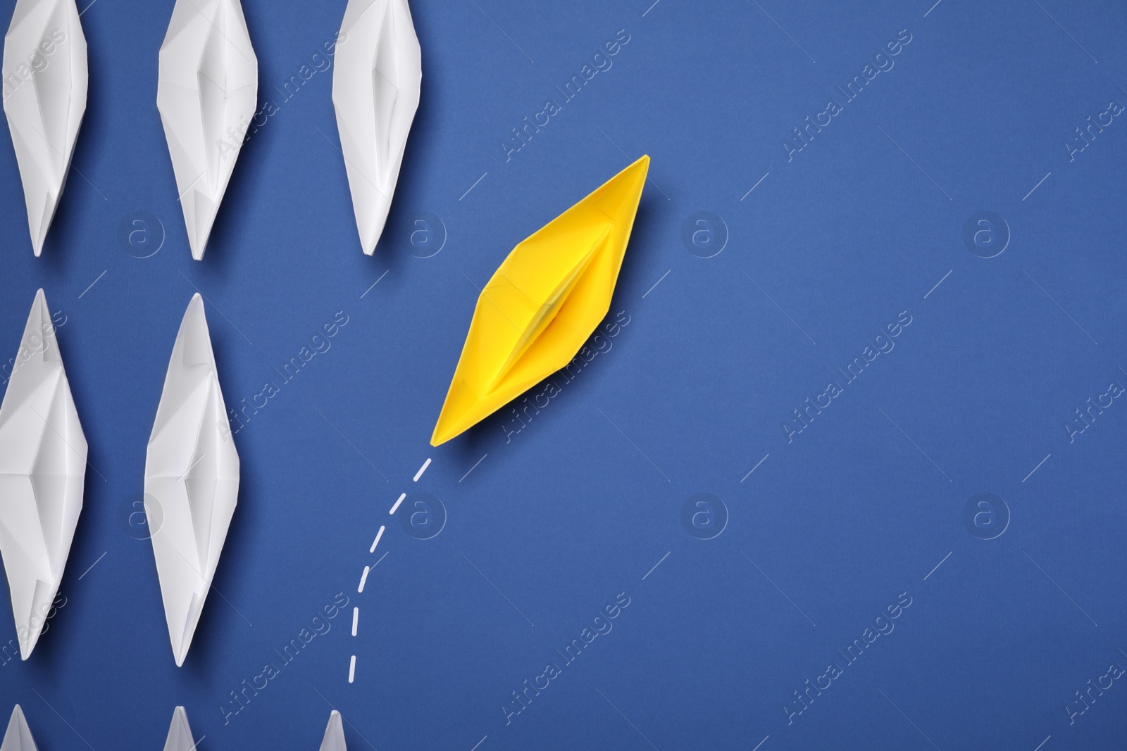 Photo of Yellow paper boat floating away from others on blue background, flat lay with space for text. Uniqueness concept