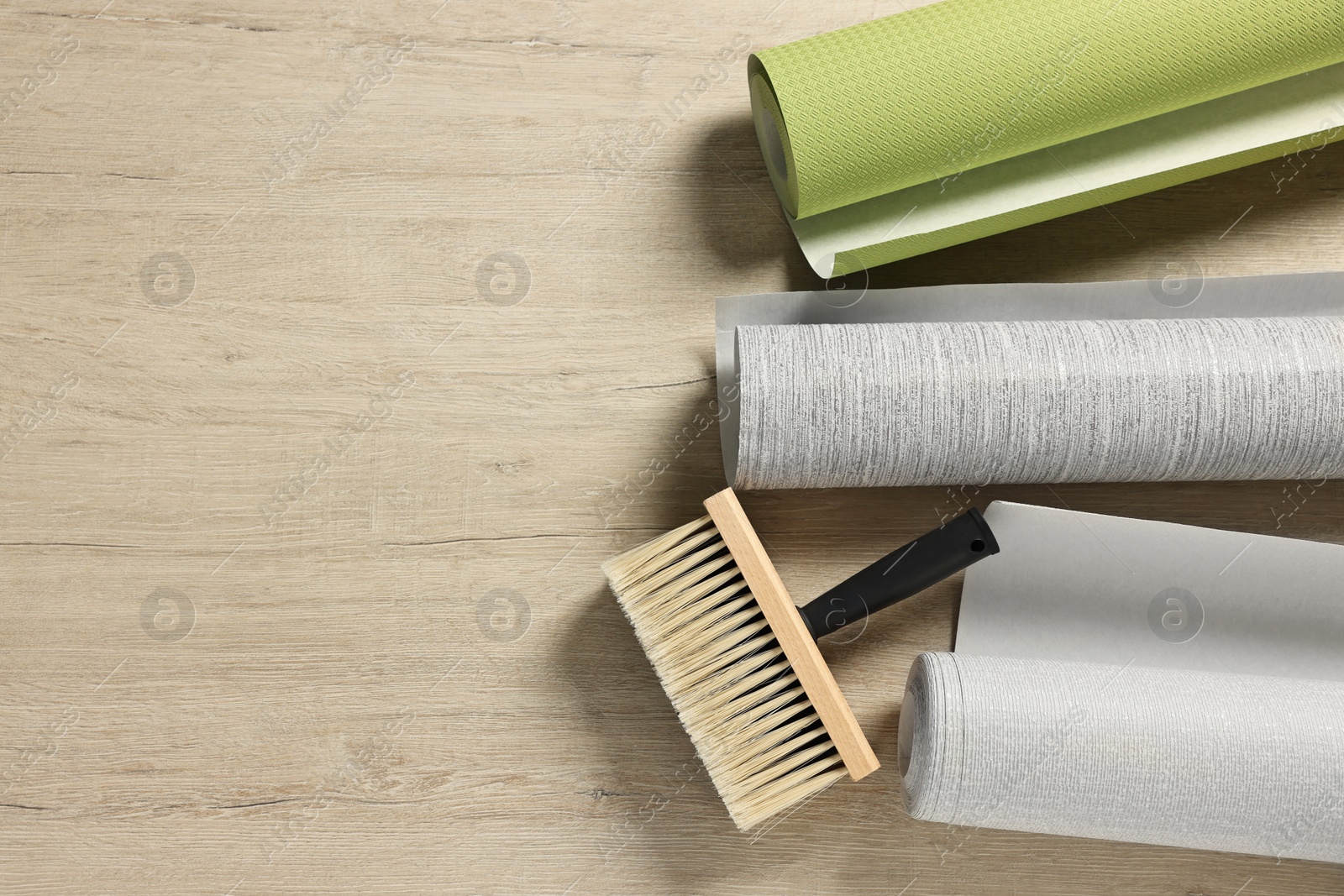 Photo of Different wallpaper rolls and brush on wooden table, flat lay. Space for text