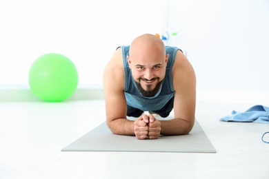 Overweight man doing plank exercise on mat in gym