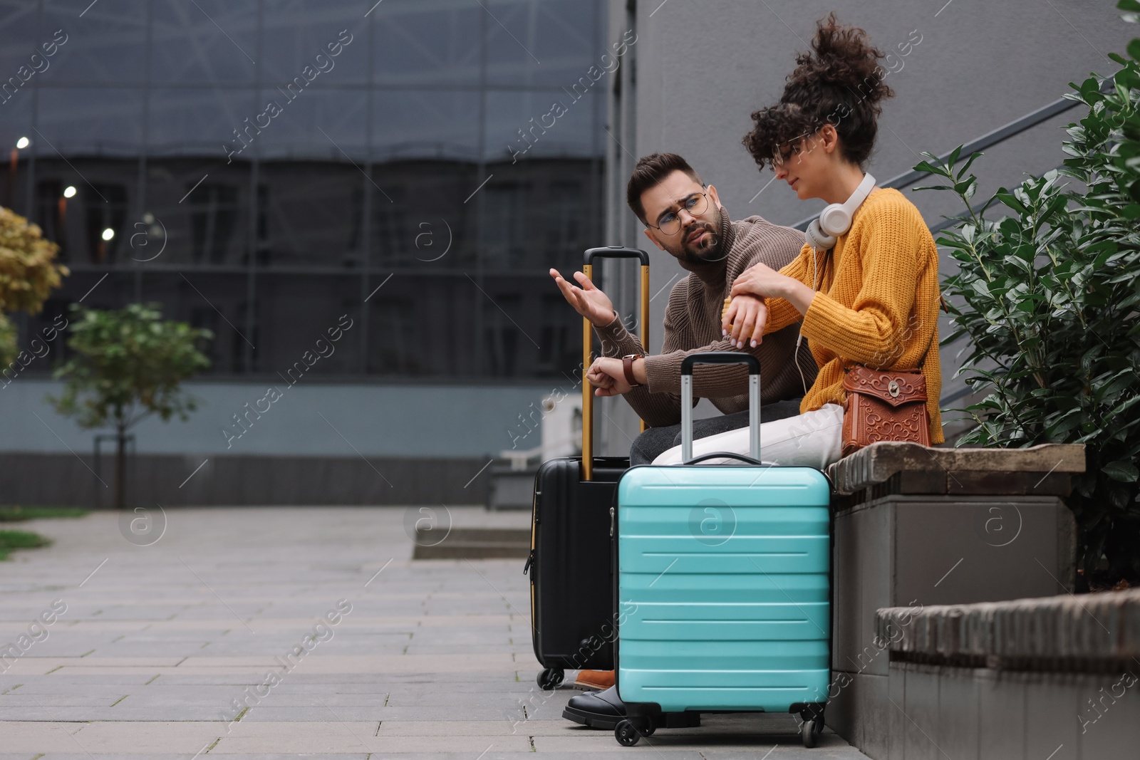 Photo of Being late. Woman and man with suitcases sitting on bench outdoors, space for text