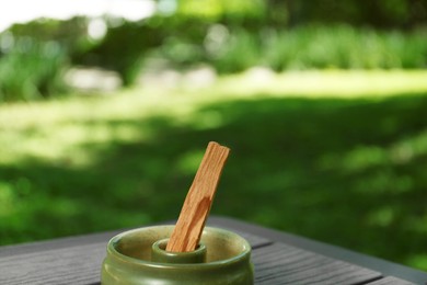 Photo of Palo santo stick in holder on wooden table outdoors. Space for text