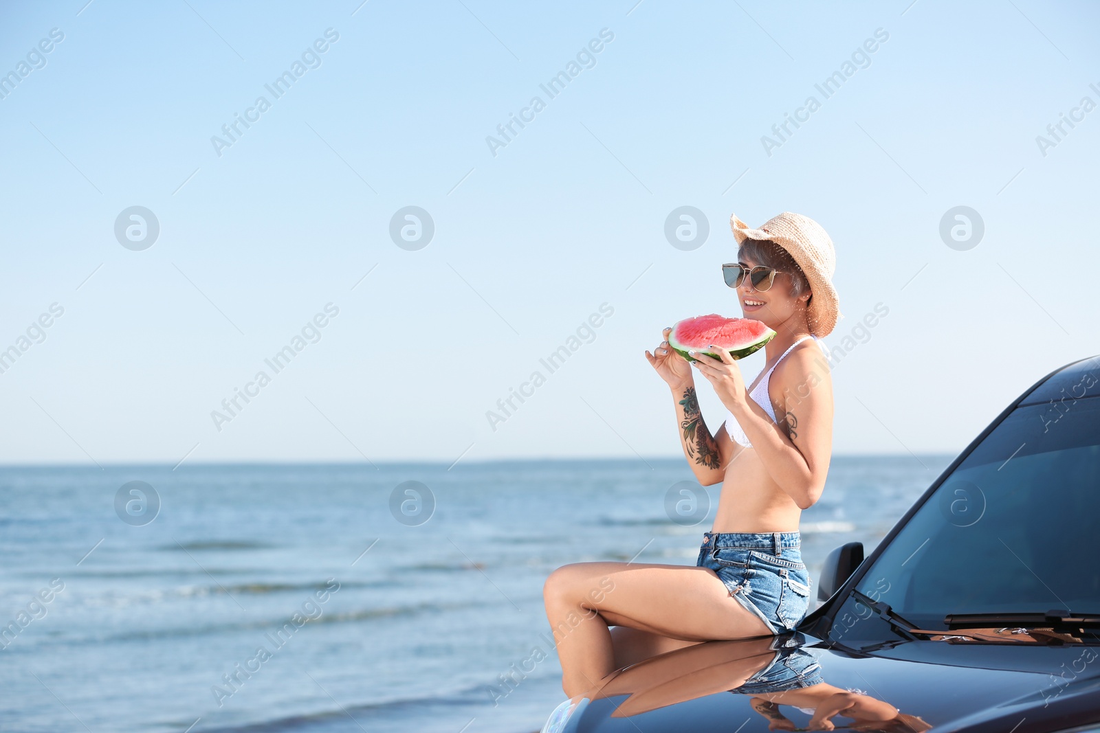 Photo of Young woman with watermelon slice near car on beach. Space for text